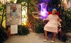 Cụ bà quá cố mặc váy cưới, ngồi ghế gỗ tại lễ tang của chính mình