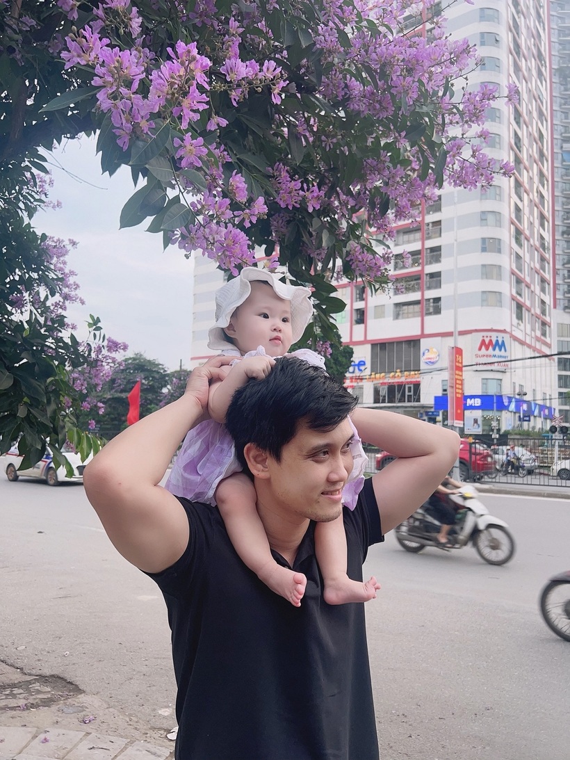 Em bé được bố cõng trên vai "đu trend" chụp ảnh với hoa bằng lăng.