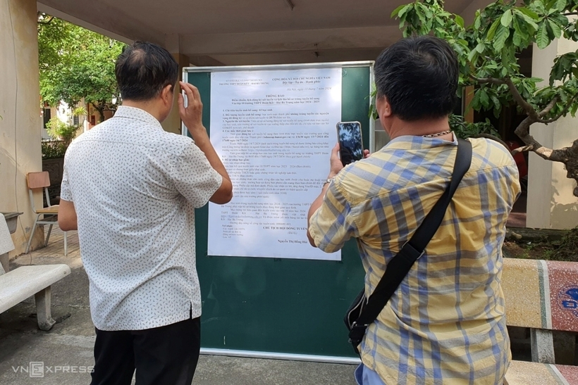 Các phụ huynh đọc thông báo của nhà trường về việc đăng ký và xét tuyển bổ sung theo hình thức trực tuyến. Ảnh: VnExpress