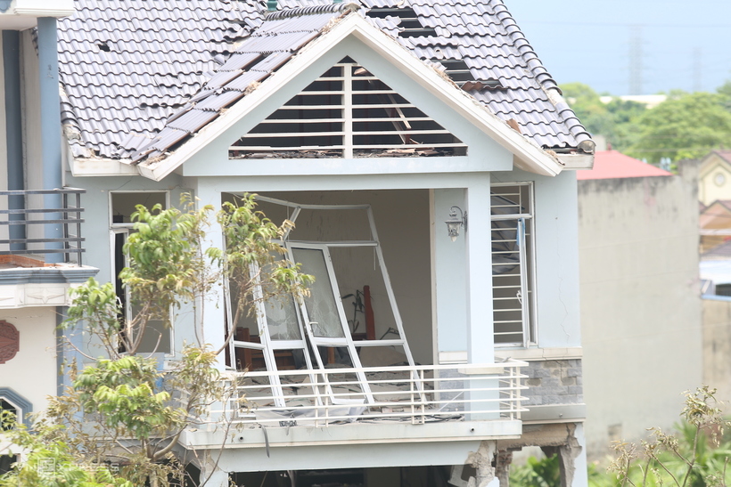 Cửa kính tầng ba của ngôi nhà bị vỡ, tung bản lề, phần khung đổ vào phía trong, mái nhà thủng lỗ chỗ.