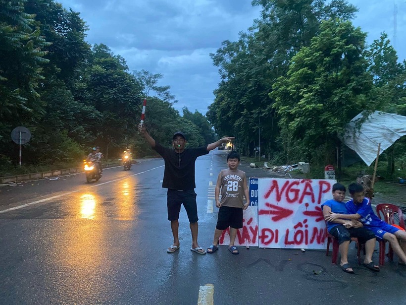 Anh Xuyên và con trai đứng chỉ đường giúp các phương tiện di chuyển tránh đường bị ngập. Ảnh: Giao Thông