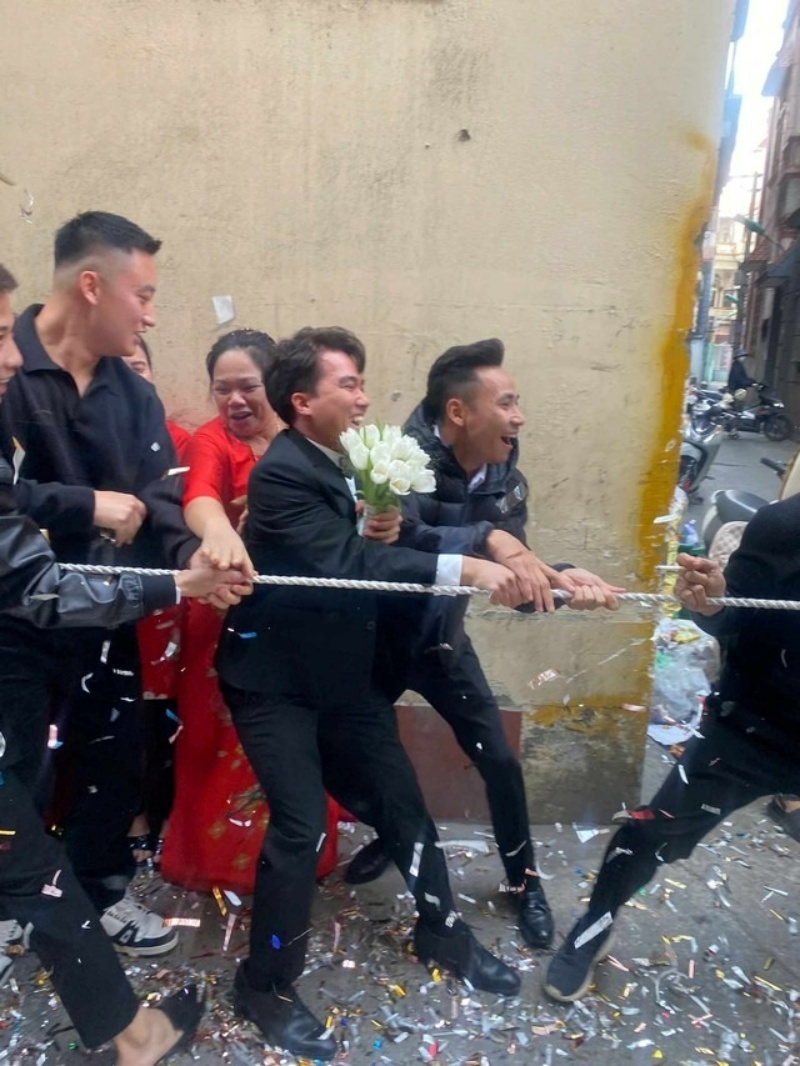 Chú rể cầm bó hoa cưới hào hứng cùng với quan viên hai họ tham gia màn kéo co trước cổng nhà cô dâu. Ảnh: Báo Thanh niên.