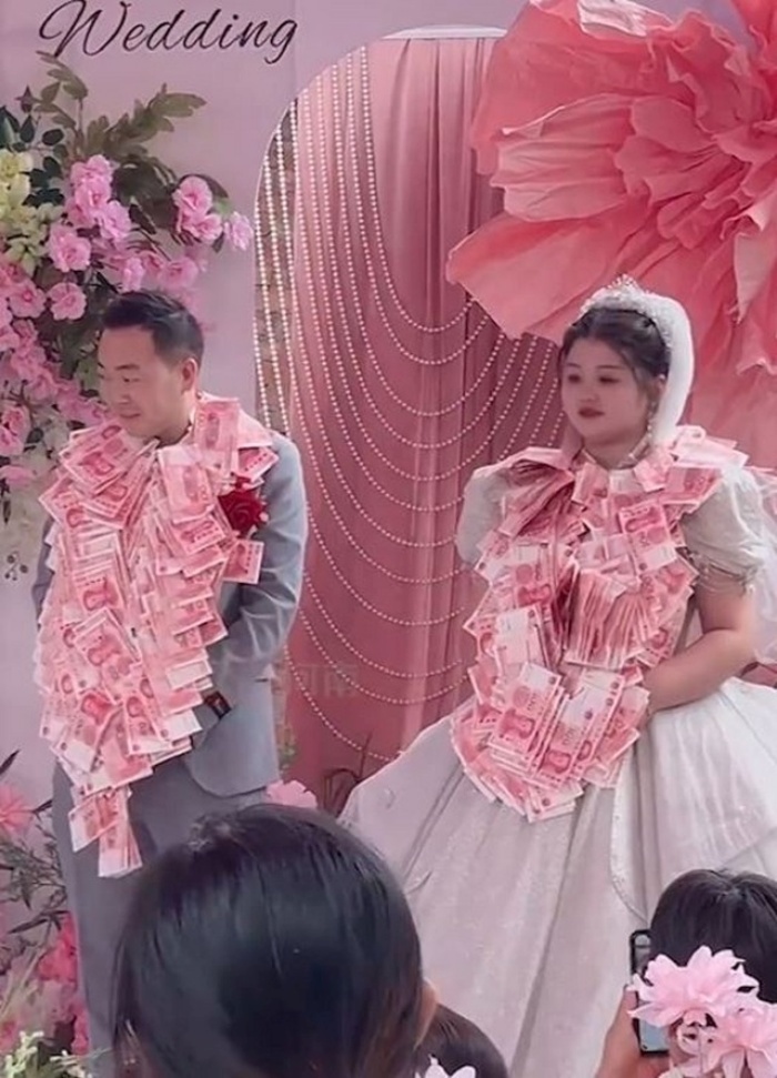 Cô dâu chú rể đứng trên sân khấu trong khi 8 cặp chị gái và anh rể thay nhau đeo những vòng hoa đầy tiền vào cổ cả hai.