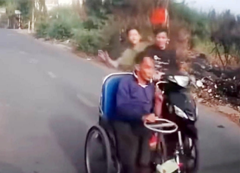 Hai thanh niên đi xe máy chạy từ phía sau đến, dùng tay tát vào đầu người đàn ông ngồi xe lăn. Ảnh: Báo Giao Thông