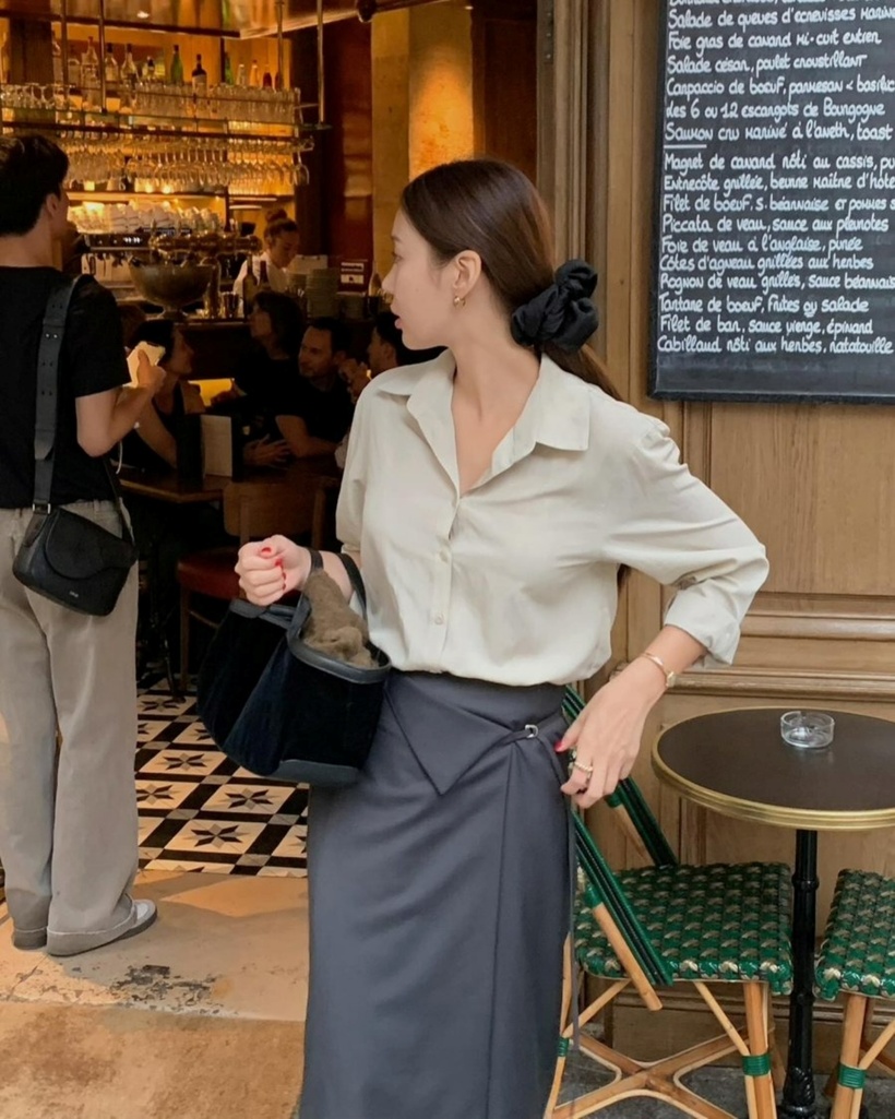 Bộ trang phục kết hợp giữa áo sơ mi và chân váy xám đậm, mặc dù có thiết kế đơn giản, nhưng vẫn mang lại sự hiện đại và trẻ trung. Khi mặc chân váy đến nơi làm việc, các chị em nên sơ vin áo để tạo nên một vẻ ngoài gọn gàng và trang nhã, phù hợp với phong cách thanh lịch nơi công sở.