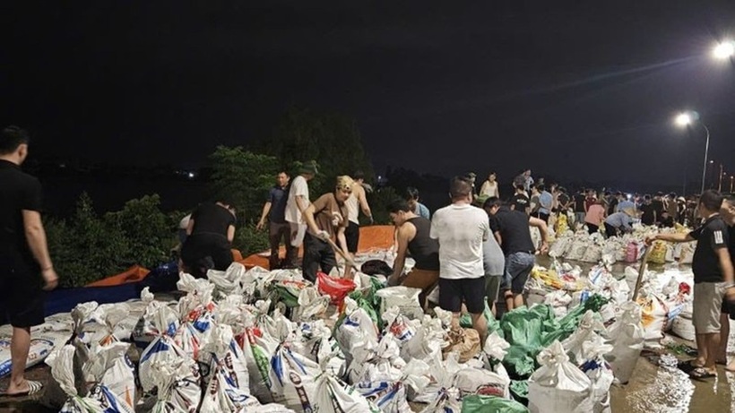 Lực lượng chức năng và người dân địa phương triển khai đắp đê bằng bao tải cát kết hợp bạt chắn sóng.