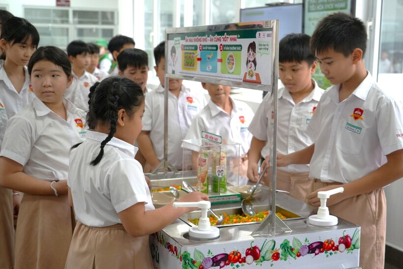 Các em học sinh xếp hàng chờ đến lượt lấy rau củ từ quầy buffet rau trong giờ ăn trưa.