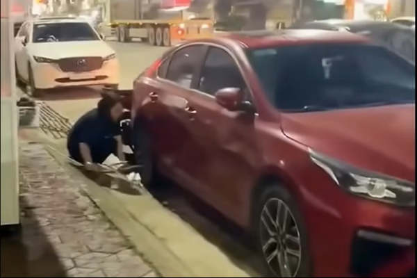 Người phụ nữ khóa bánh ô tô vì đỗ trước cửa hàng ở Hải Phòng. Ảnh: Báo Công an Nhân dân.