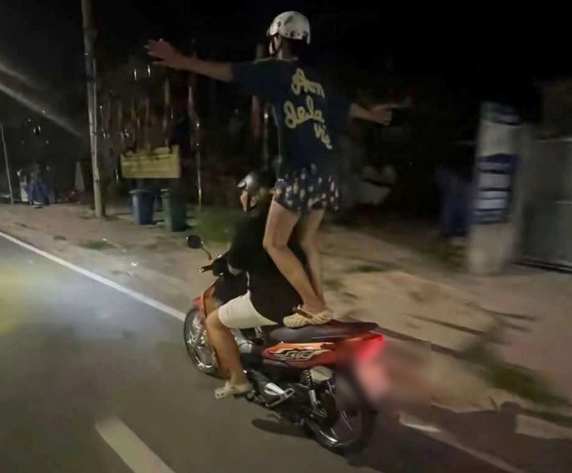 Một học sinh vừa lái xe máy, một em còn lại đứng lên yên xe dang tay trong khi xe đang chạy. Ảnh: Thanh niên