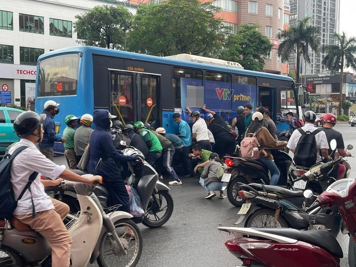 Hàng chục người nâng xe buýt để cứu người phụ nữ kẹt dưới gầm - Ảnh: D.C./ Theo Tuổi trẻ online