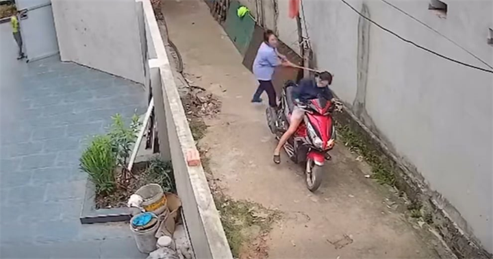 Người phụ nữ áo xanh cầm chổi đập mạnh vào đầu hàng xóm. (Ảnh cắt từ clip)